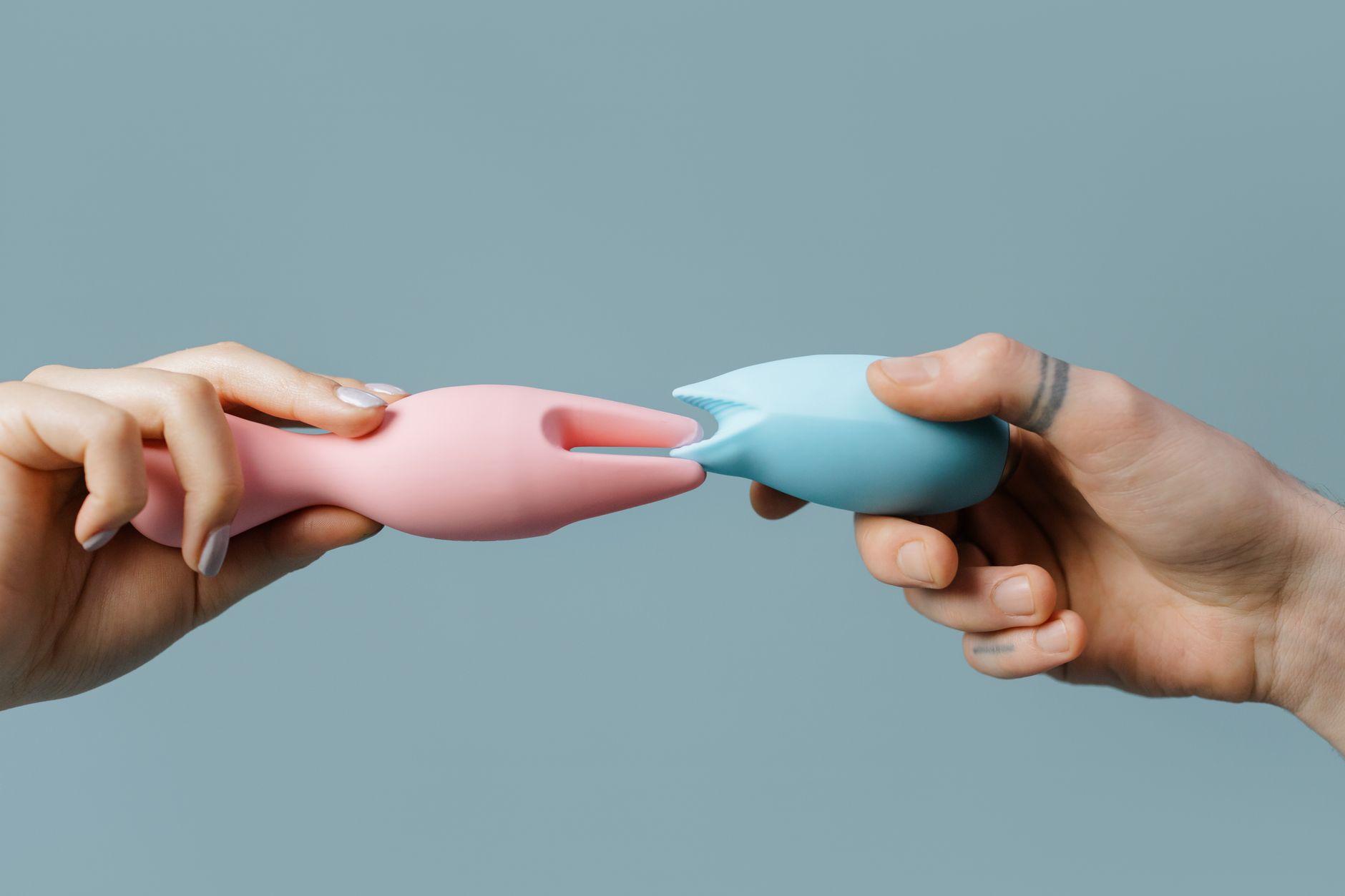 Mani che tengono vibratori colorati in silicone su superficie neutra, simbolo di esplorazione senza ansia