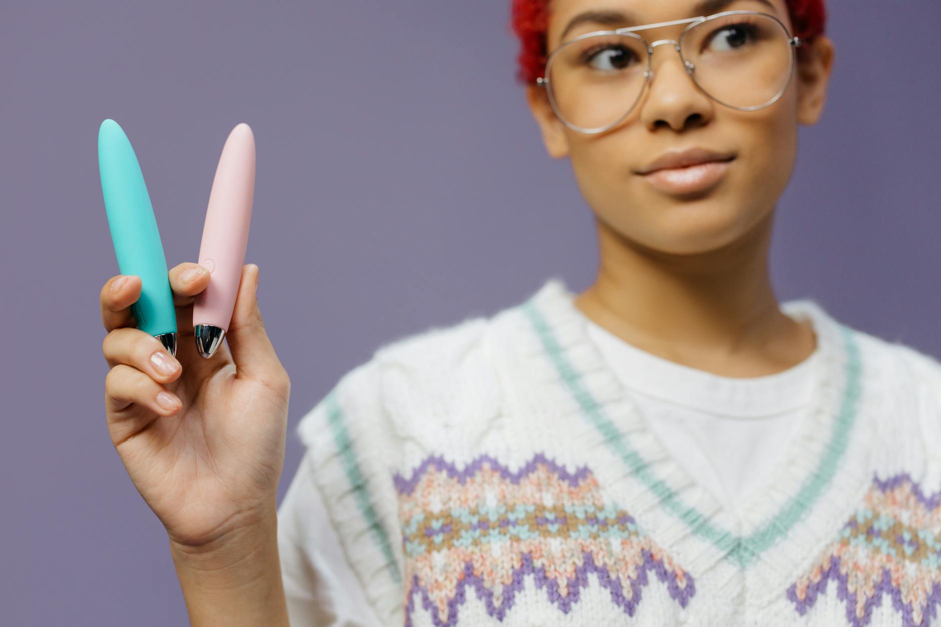 Una donna con occhiali che tiene due vibratori colorati in modo contemplativo