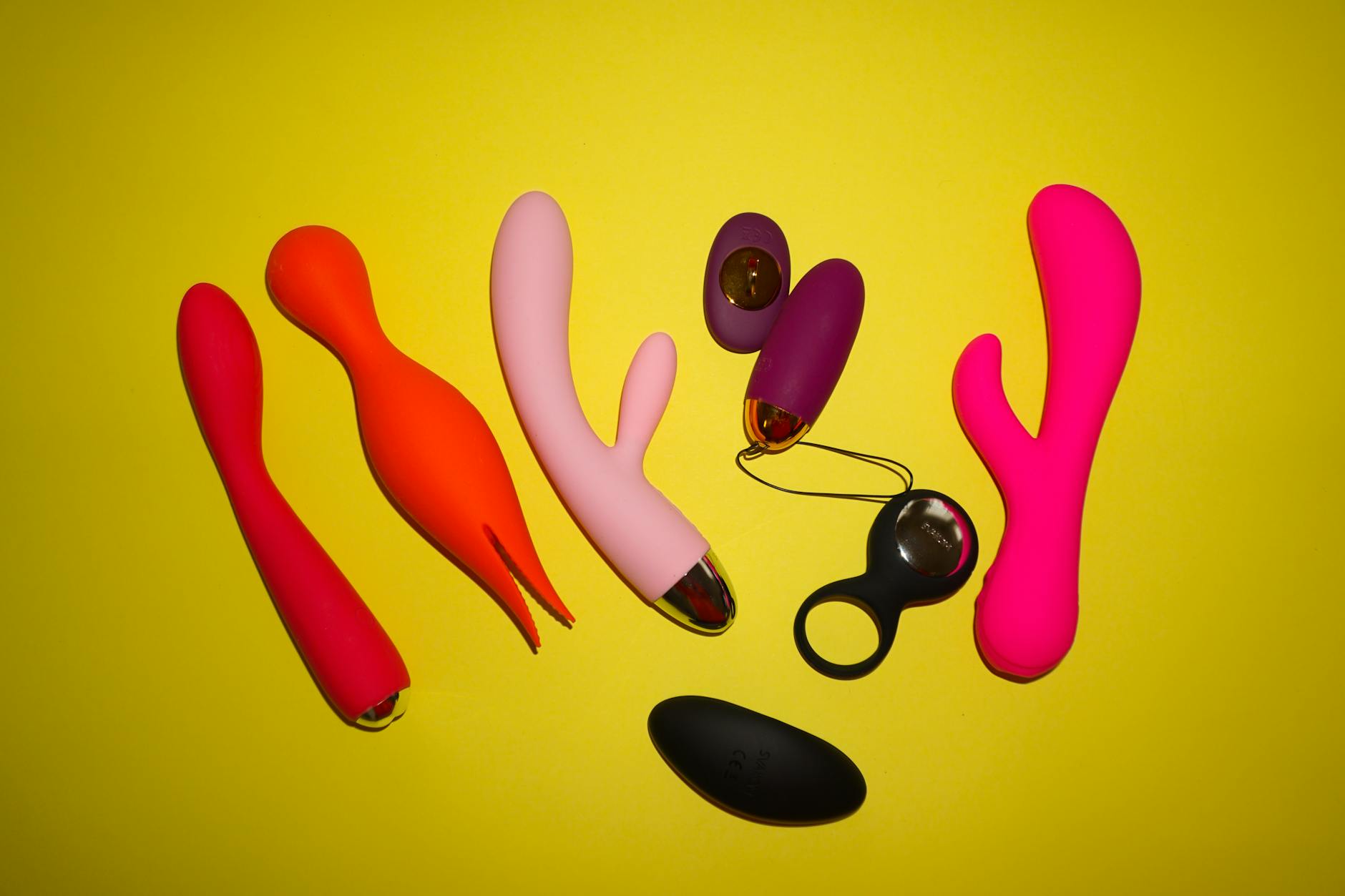 Woman holding two colorful vibrators against a purple background, representing choice and exploration
